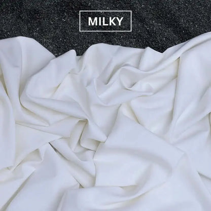 Soft milky white fabric draped on dark textured surface with MILKY label above